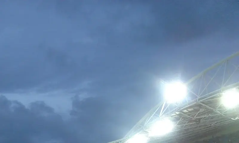Projecteurs allumés sur le toit d'un stade, sous un ciel d'orage
